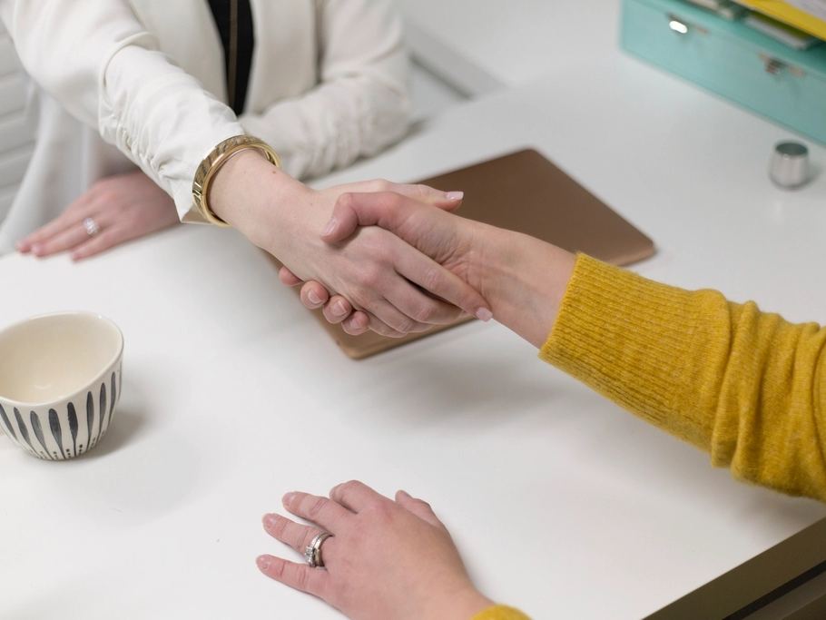 Two people shaking hands across a desk after a meeting